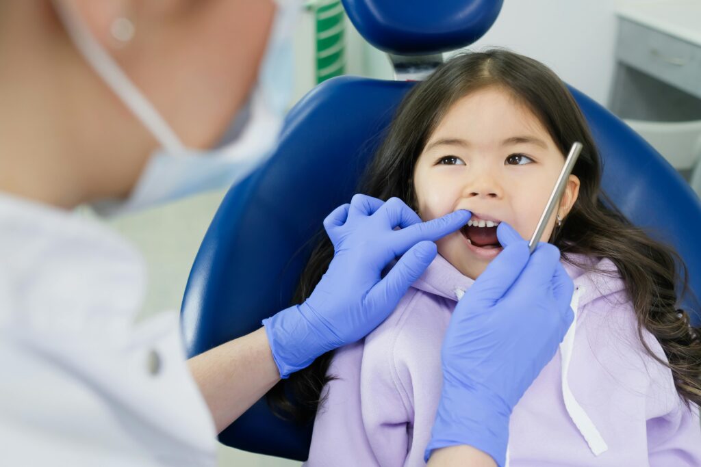 A dentist in Valdosta wearing blue gloves examines a young girl’s teeth as she sits in a dental chair.